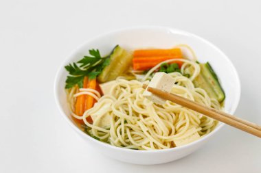 Beyaz arka planda tofu peyniri, erişte, havuç ve kabak ile geleneksel asya çorbası. Bu yemek genellikle bulyon ve sebze içerir