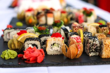 Koyu bir kayrak plaka üzerinde vasabi ve zencefil ile suşi rulo seti, Büfe tablo, yatay oryantasyon, yakın