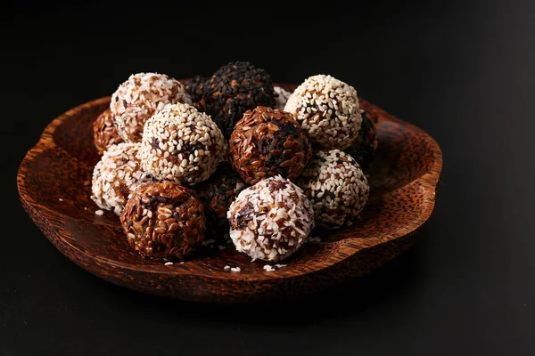 Bolas de energía de frutos secos, avena y frutos secos sobre una placa de coco de madera sobre un fondo oscuro, orientación horizontal — Foto de Stock