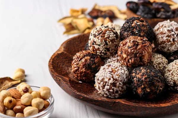 Bolas energéticas saludables de frutos secos, avena y frutas secas con semillas de coco, lino y sésamo sobre un plato de madera de coco sobre un fondo blanco, orientación horizontal, primer plano — Foto de Stock