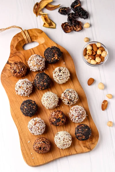 Gesunde Energiebällchen aus Nüssen, Haferflocken und Trockenfrüchten mit Kokos, Flachs und Sesam auf Holzbrett auf weißem Hintergrund, vertikale Ausrichtung, Draufsicht — Stockfoto