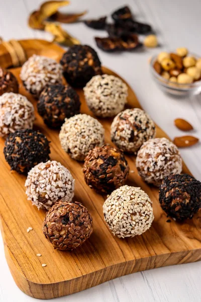 Boules énergétiques saines de noix, flocons d'avoine et fruits secs avec graines de noix de coco, lin et sésame sur planche de bois sur fond blanc, orientation verticale, vue de dessus — Photo