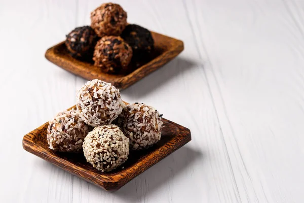 Bolas energéticas saludables de frutos secos, avena y frutos secos con semillas de coco, lino y sésamo sobre platos de coco de madera sobre fondo blanco, orientación horizontal — Foto de Stock