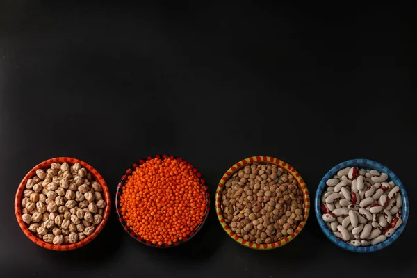 Röda och bruna linser, kikärter och vita bönor är baljväxter som innehåller mycket protein ligger på en mörk bakgrund i skålar, horisontell orientering, uppifrån — Stockfoto