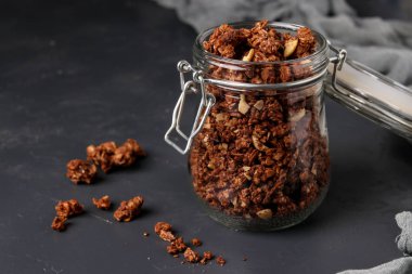 Doğal bal, çikolata ve fındık ile granola gevrek müsli koyu bir arka plan, sağlıklı gıda, yatay yönelim karşı cam bir kavanozda
