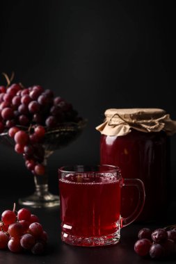 Bir bardak ve bir can- ı üzüm suyu, bir meyve sıkacağı pişmiş, koyu arka plan, dikey yönelim, yakın çekim yerel bir üzüm hasat suyu hasat
