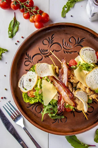 Salade César et brochettes de poulet sur une assiette brune sur fond blanc, orientation verticale, vue sur le dessus — Photo