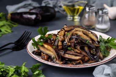 Fried eggplants with garlic and soy sauce, sliced in stripes, in a plate against a dark background clipart