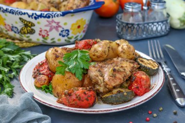 Tavuk uyluk patates, domates ve kabak ile pişmiş, bir tabak ve seramik şeklinde bulunan, koyu bir arka plan üzerinde, yatay yönelim