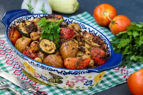 Куриные бёдра, запеченные с картошкой, помидорами и цуккини, расположены в керамической форме на тёмном фоне, горизонтальная ориентация — стоковое фото