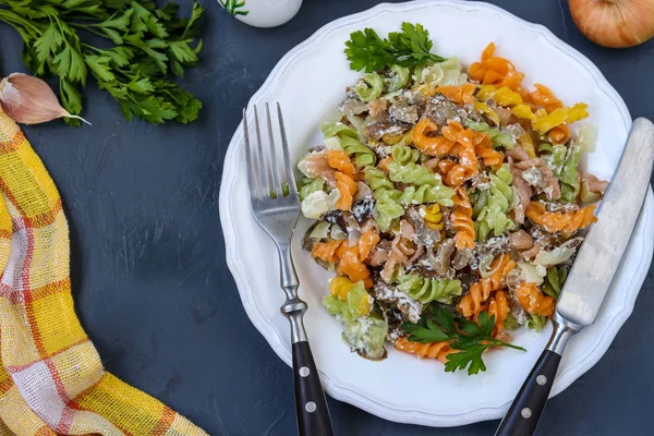 Fusilli multicolored pasta with vegetables in a white plate on dark background, top view, horizontal orientation