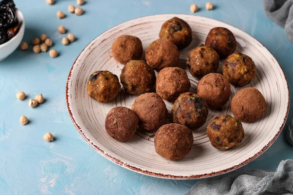 Bolas de energía de garbanzo, ciruelas pasas y dátiles, espolvoreadas con cacao en un plato sobre un fondo azul claro, orientación horizontal, vista superior — Foto de Stock