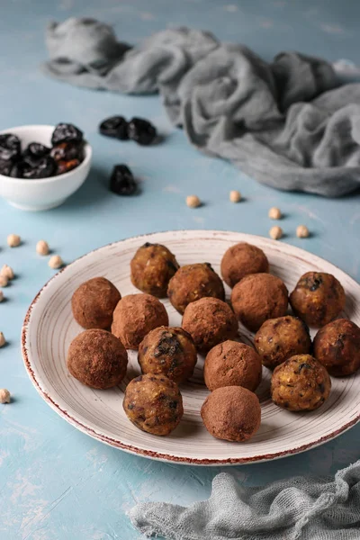 Bolas de energía de garbanzo, ciruelas pasas y dátiles, espolvoreadas con cacao en un plato sobre un fondo azul claro, orientación vertical, vista superior — Foto de Stock