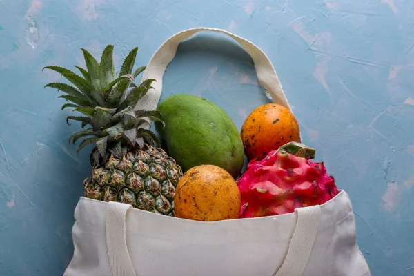 Zero waste concept, Shopping textile bag with fresh tropical fruits: mango, pineapple, dragon and passion fruit on light blue background, top view
