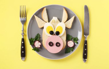 Komik bir boğa şeklinde sosisli ve yumurtalı sandviç, sarı arka planda yeni 2021 'in sembolü, çocuklar için aşçılık fikri, yassılaşma