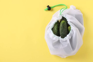 Parlak sarı arka planda, yeniden kullanılabilir çevre dostu ağ çantasındaki salatalıklar. Sıfır atık konsepti, kirliliği durdurun. Boşluğu kopyala