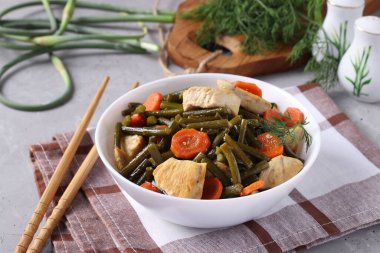 Fried chicken with garlic arrows, carrots and soy sauce in a white plate on a gray concrete background, horizontal format, closeup