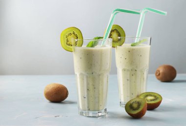 İki sağlıklı detoks smoothie kivi ve muz uzun bardaklarda açık mavi zemin üzerinde taze malzemelerle, diyet ve kilo kaybı konsepti