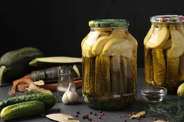 Gemarineerde komkommers en courgettes in potten op donkere achtergrond, oogst voor de winter, horizontaal formaat — Stockfoto