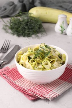 Dereotu, sarımsak, gri arka plan, dikey formatta ince kurdeleler halinde kesilmiş genç kabak atıştırmalıkları.