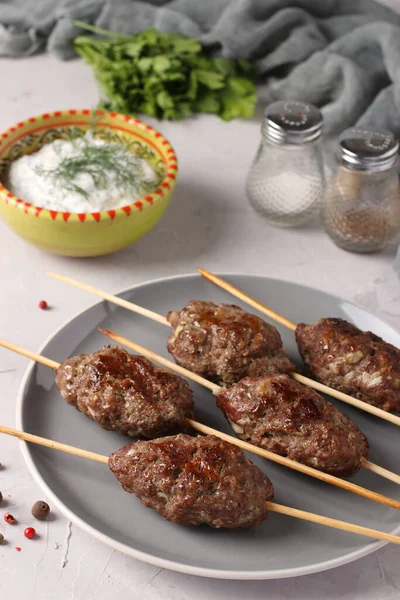 Kofta kebab on wooden skewers on a plate and sauce on the table, traditional dish of Arab cuisine, grilled minced meat shish kebab, Vertical format