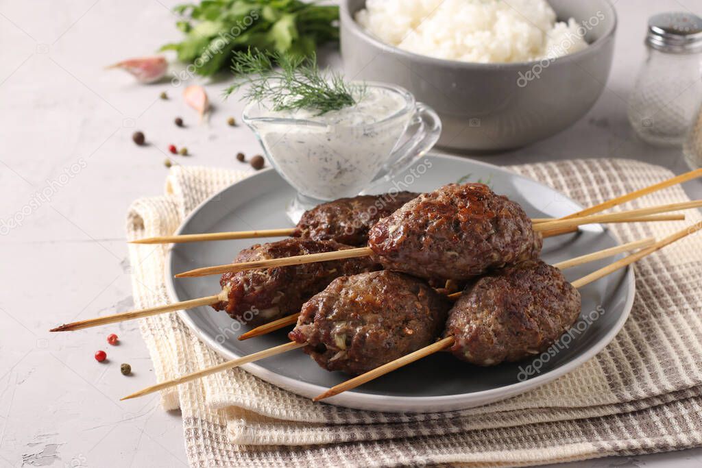 Kofta kebab on wooden skewers on a plate with sauce and a side dish of rice on the table, traditional dish of Arab cuisine, grilled minced meat shish kebab, Closeup