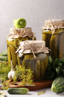 Açık gri arka planda cam kavanozlarda sarımsak, biber ve dereotlu marine edilmiş salatalıklar, dikey format.