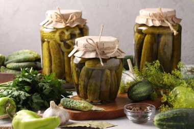 Açık gri arka planda cam kavanozlarda sarımsak, biber ve dereotlu ev yapımı salatalıklar, yatay formatta.