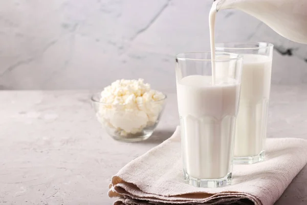 Kefir oder Ayran fermentiertes Getränk wird in ein Glas aus einem Krug gegossen, sowie Quark in einer Schüssel auf hellgrauem Hintergrund, Nahaufnahme, Platz für Text — Stockfoto