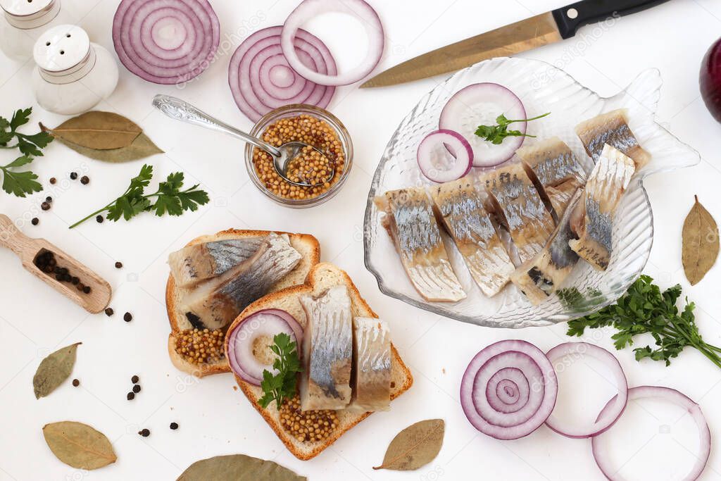 Snack from salted herring on bread with red onion and mustard on white background