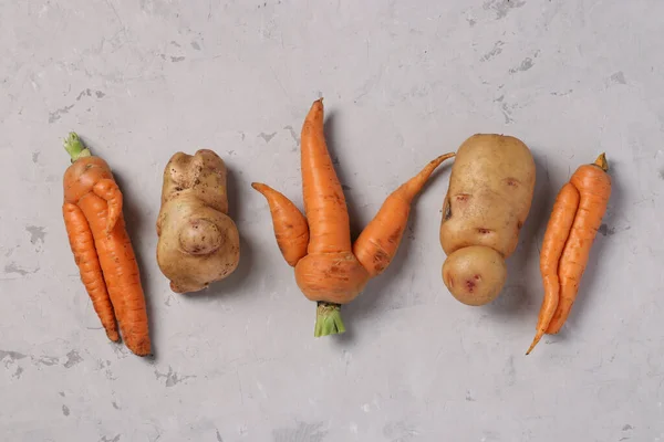 Patatas y zanahorias orgánicas feas de moda sobre fondo gris, concepto de comida fea, formato horizontal, vista superior — Foto de Stock