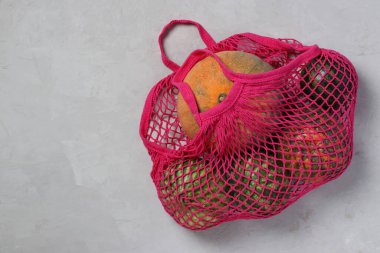 Rengarenk balkabakları ve fuşya renginde küçük karpuzlar açık arkaplanda ağ torbası, sıfır atık kavramı, üst manzara. Metin için boşluk