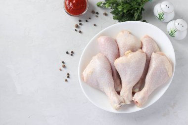 Açık gri zemin üzerinde beyaz tabakta çiğ tavuk budu, Üst görünüm, Yatay biçim, metin için boşluk