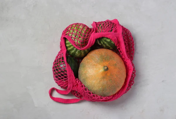 Various colorful pumpkins and small watermelons in fuchsia color mesh bag on light background, Zero waste concept, View from above