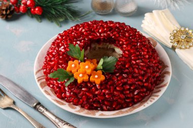 Nar tohumlarıyla süslenmiş salata narlı bileziği ve açık mavi arka planda havuç çiçekleri. Geleneksel Rus Yeni Yıl Salatası, Yakın plan, Yukarıdan Görünüm