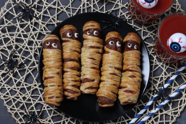 Karanlık tabakta Cadılar Bayramı partisi için ürkütücü sosisli mumyalar ve domates suyu..