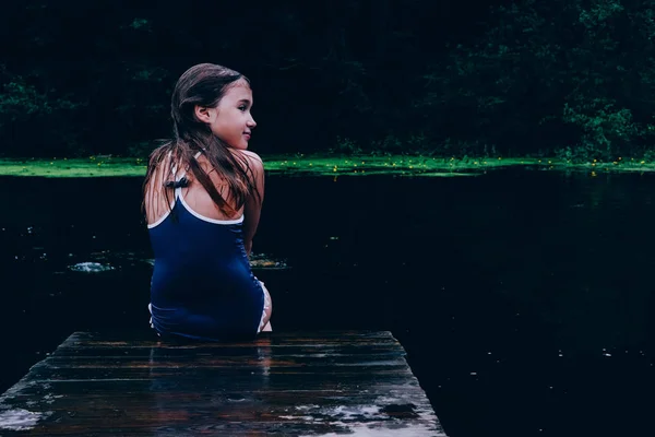 Menina sentada no cais olhando para trás — Fotografia de Stock