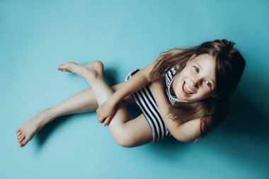 Düz mavi arka plandaki çocuk kameraya bakarak oturuyor