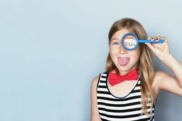 Jong meisje geven kijken door vergrootglas portret op grijze achtergrond — Stockfoto