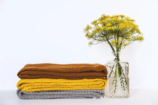 Stack of clean dry towels and vase with plants on table