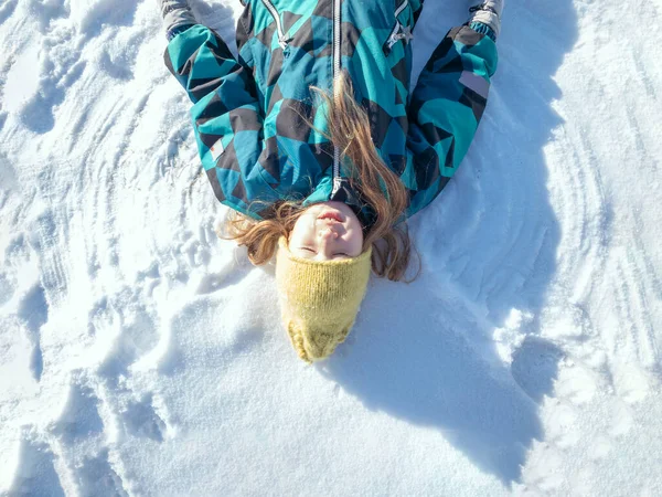Mutlu kız karda yatıyor ve kar meleği figürü yapıyor. — Stok fotoğraf