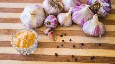 Kahverengi ahşap bir tahtanın üzerinde biber ve sarımsak çeşnili güzel ve büyük bir sarımsak var..