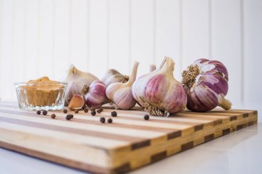 Kahverengi ahşap bir tahtanın üzerinde biber ve sarımsak çeşnili güzel ve büyük bir sarımsak var..