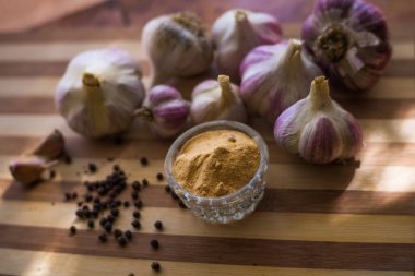 Kahverengi ahşap bir tahtanın üzerinde biber ve sarımsak çeşnili güzel ve büyük bir sarımsak var..