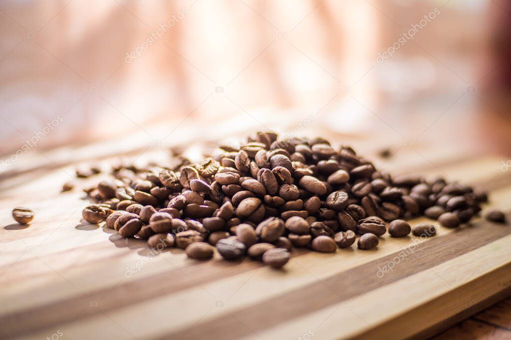 Roasted arabica coffee beans are scattered on a wooden plank.