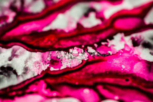 Black and pink refill ink spilled onto the white sink and the ink mixed into abstract blobs and patterns.