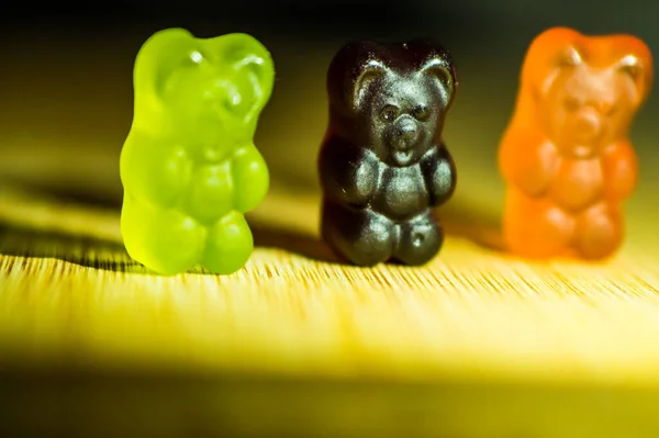 Sweet gummy bears stand on a wooden background, behind the shadow on a wooden plank of gummy bears. Gummy bears are in a row.