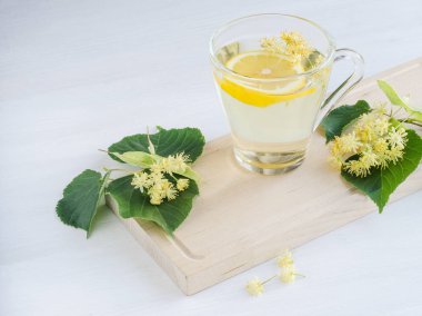 Şeffaf bir fincan çay limon ve ıhlamur çiçek bir ahşap tahta üzerinde duruyor. Yaprak ve çiçek Linden, çevresinde bulunmaktadır.