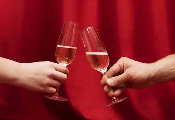 Hands Man and woman sitting at a table with glasses of champagne. red background — Stock Photo, Image