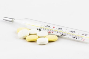 Termometre ve birçok tablet beyaz arkaplana yakın çekim yapıyor. Soğuk algınlığı, grip, mevsim, sonbahar, kış, bağışıklık